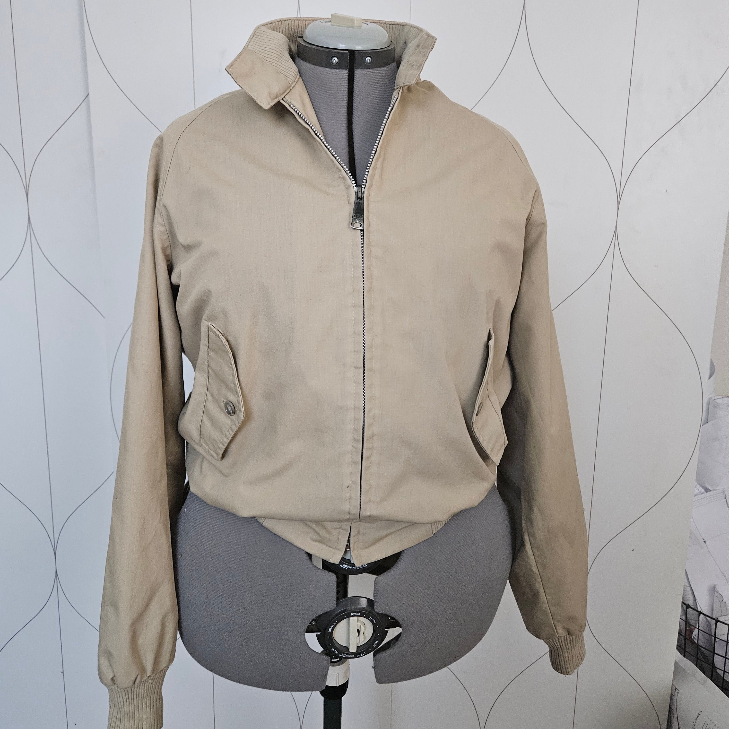 Front of a beige jacket with ribbed collar, metal zipper, and button pockets