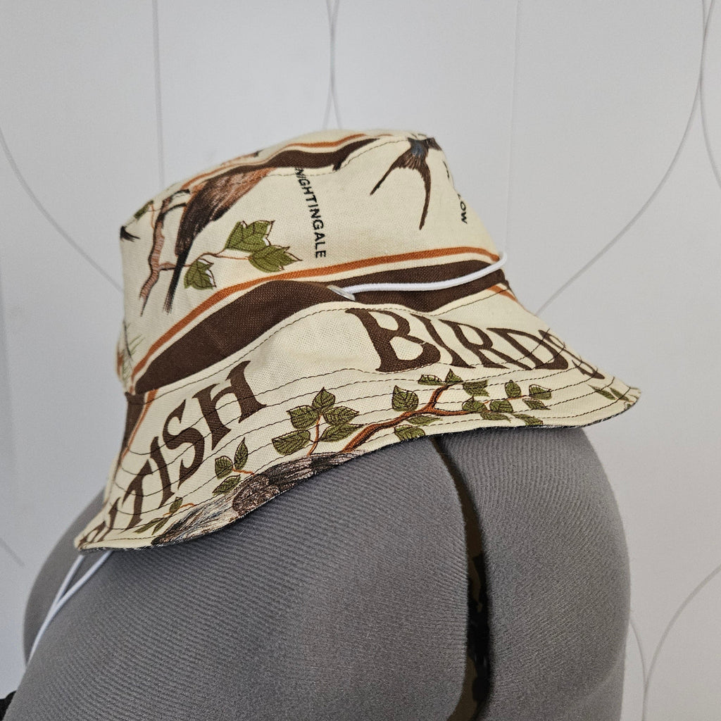 A gray mannequin displaying a hat with cream-colored brim featuring brown stripes and green leaves, showing the words 'British Birds'