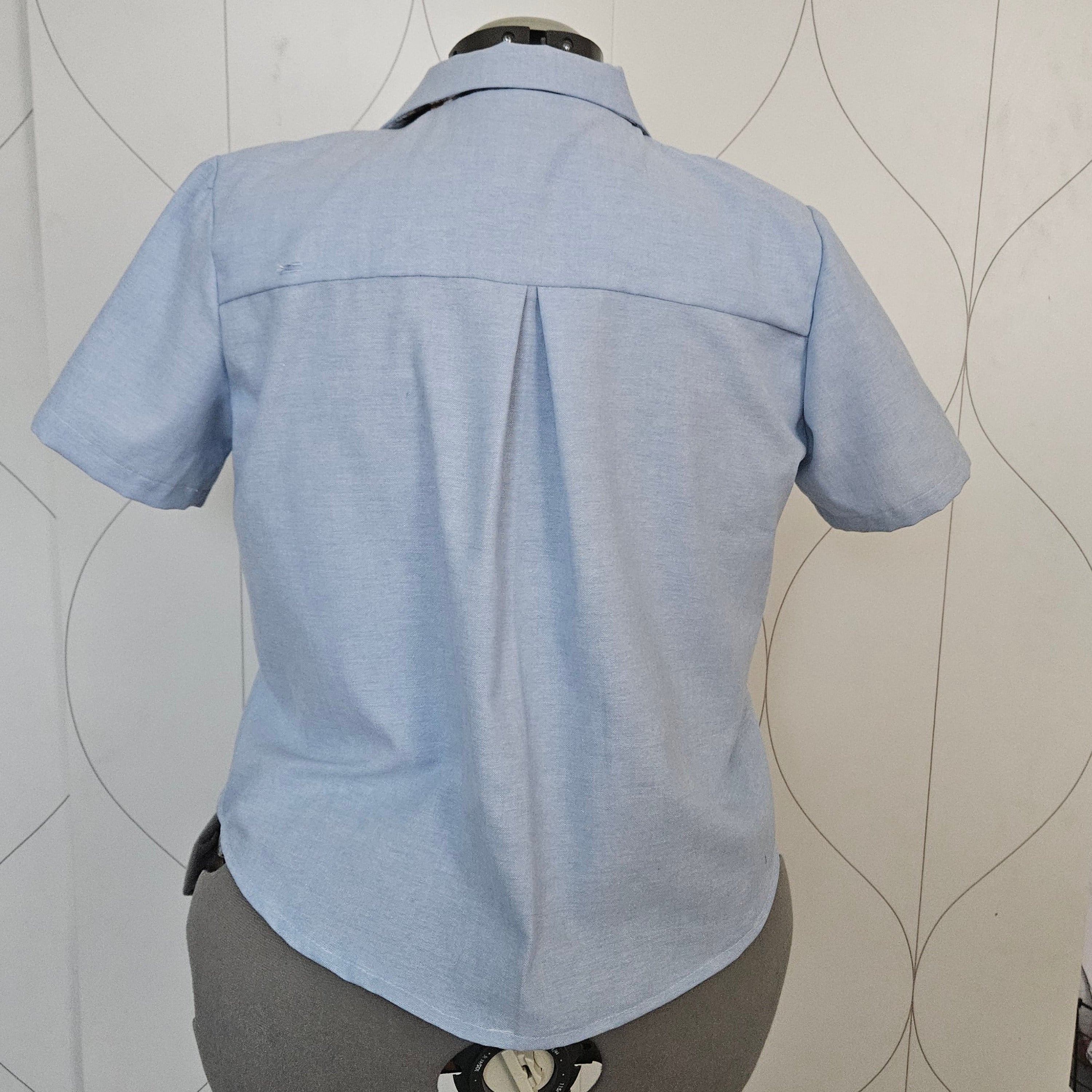 Back view of light blue shirt with collar, back yoke, and inverted box pleat