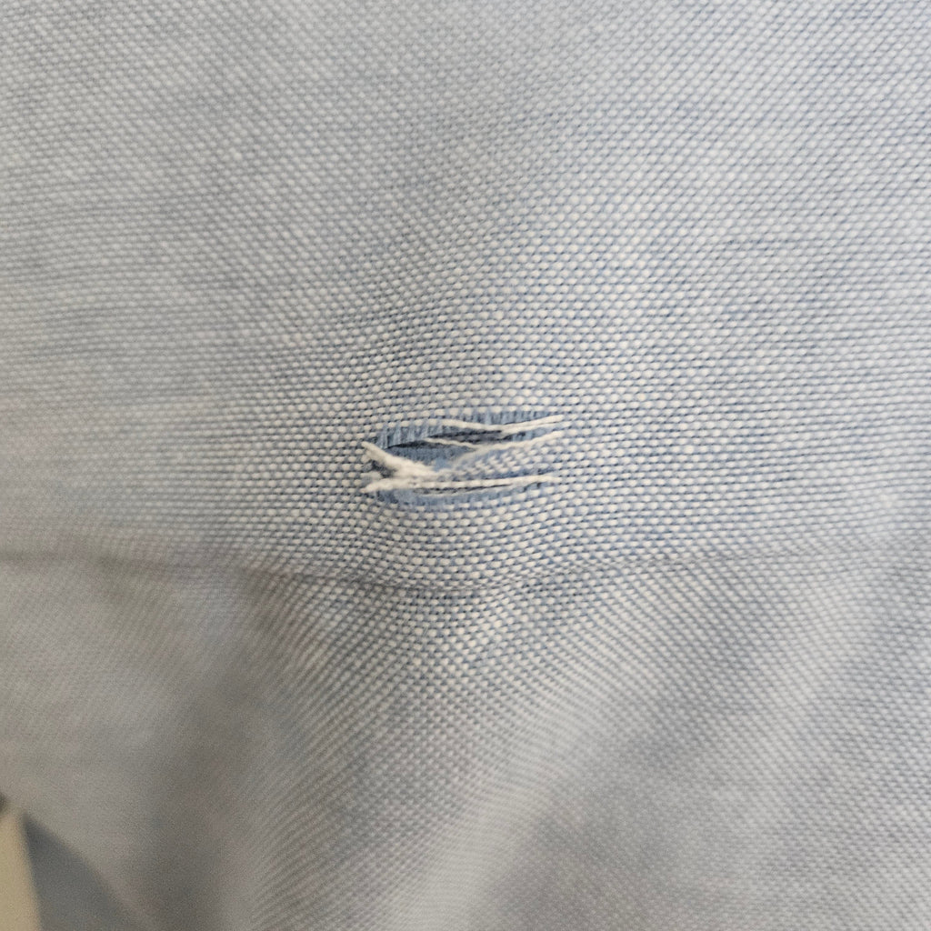 Close-up of small hole on the back of light blue shirt