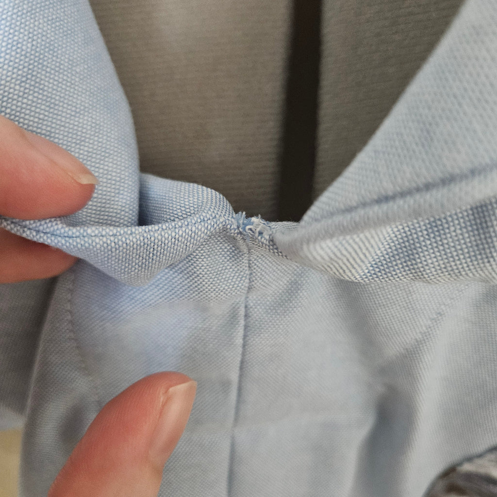 Close-up of loose threads at the point where collar pieces meet on light blue shirt