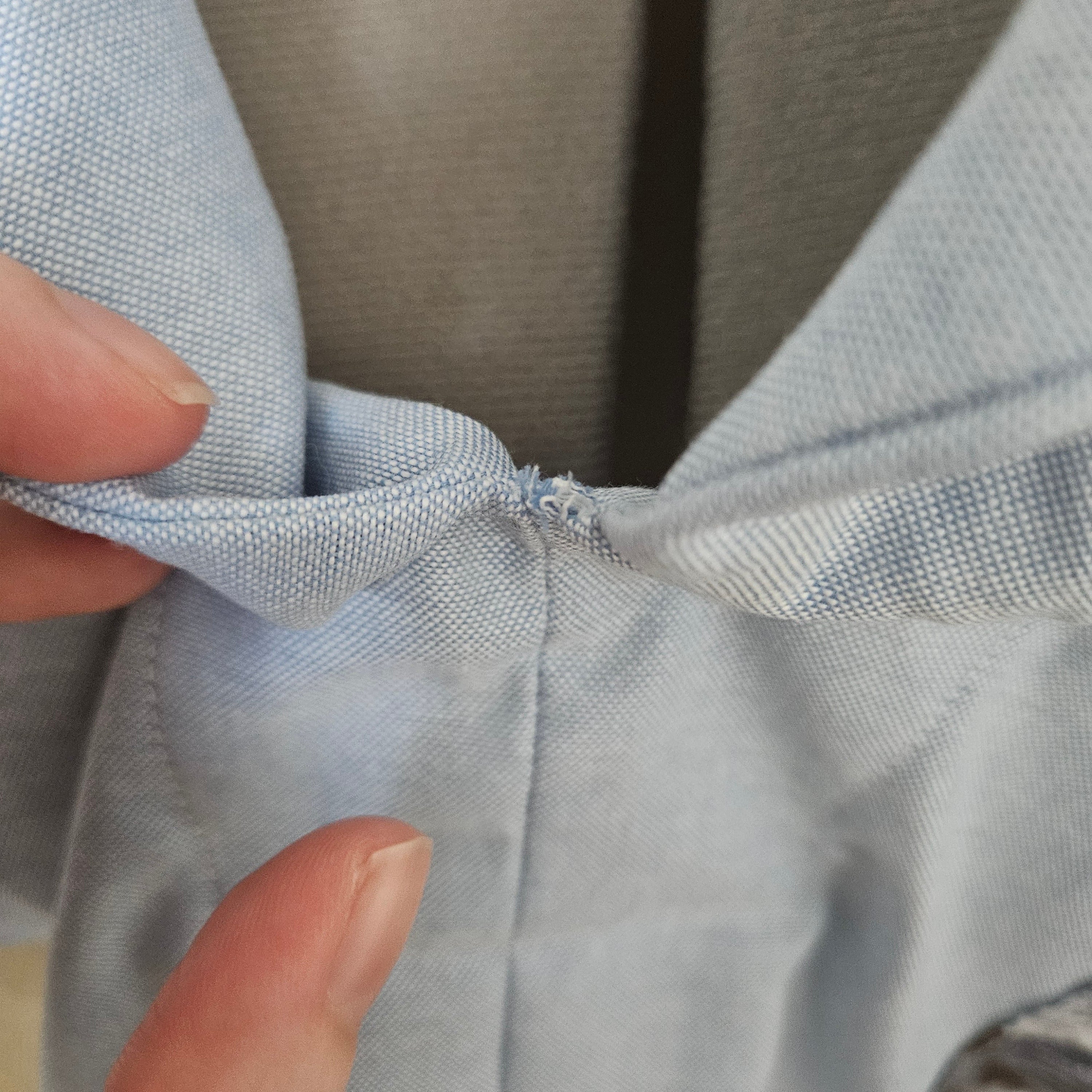 Close-up of loose threads at the point where collar pieces meet on light blue shirt